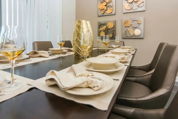 Une table à manger dressée avec des assiettes, des verres et des serviettes, entourée de fauteuils en cuir dans un intérieur moderne agrémenté d’œuvres d’art murales abstraites.