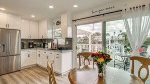 A modern kitchen with white cabinets, stainless steel appliances, and a wooden dining table with chairs. - 'Breeze by the Marina' Chula Vista Getaway! (Chula Vista)