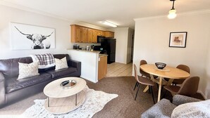 A living room with a dark leather sofa, a round coffee table, and a dining area with a wooden table and chairs.
