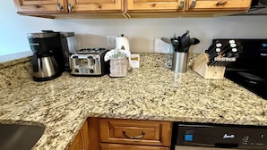 A kitchen with wooden cabinets, a granite countertop, a coffee maker, a toaster, a kettle, a knife block, and a dishwasher.