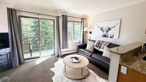 A living room with a sofa, a coffee table, a TV, and a large window with curtains.
