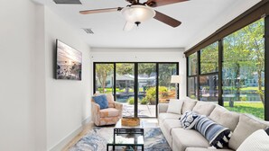 Un salon spacieux doté d’un ventilateur de plafond, de grandes fenêtres, d’un canapé, d’une table basse et d’un fauteuil.