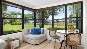 Un salon moderne avec une grande fenêtre, un canapé agrémenté d’un coussin bleu et des fauteuils en osier.