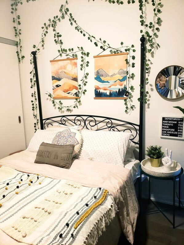 Cozy retreat with a neatly made bed, artwork, and a potted plant.