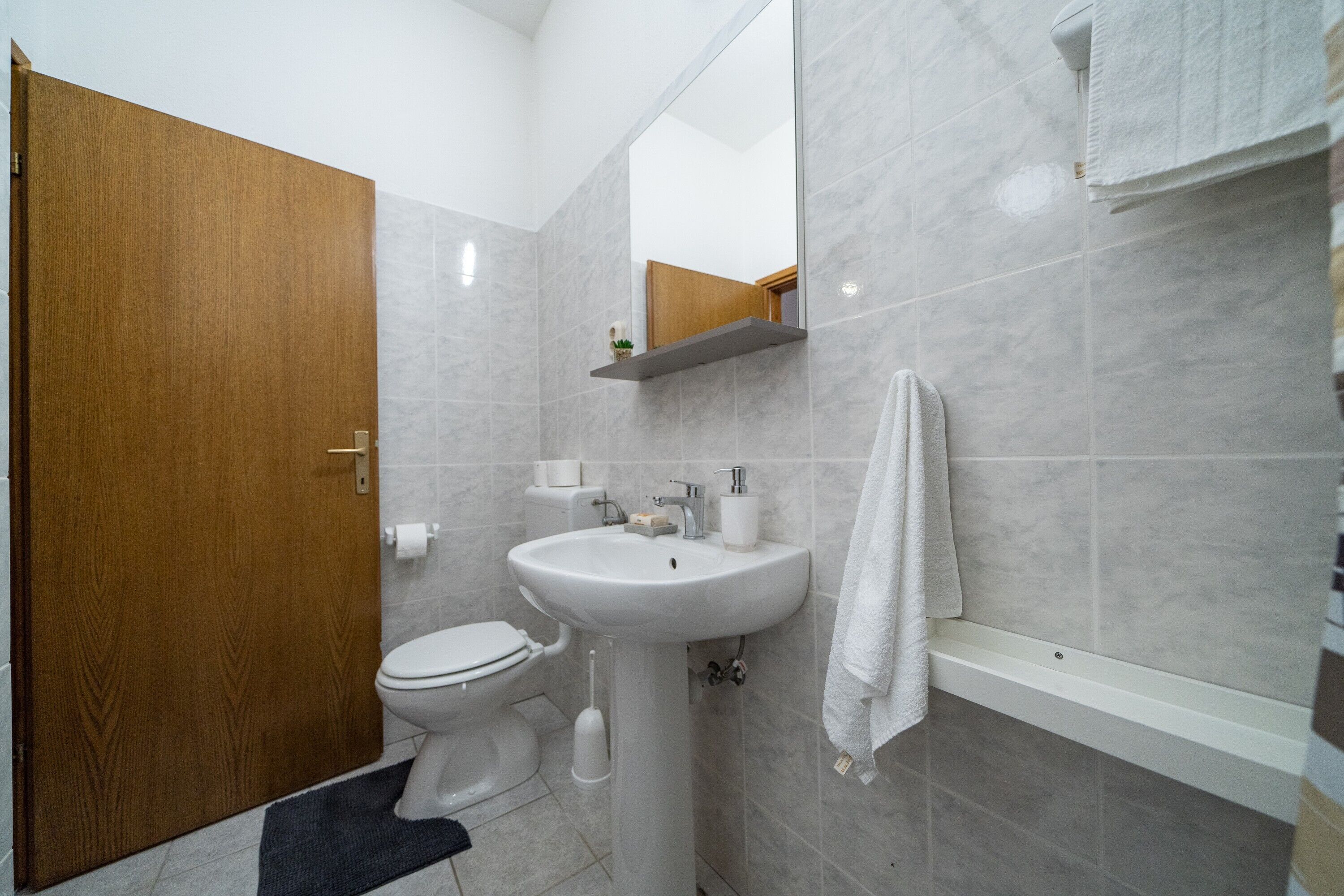 A bathroom with a toilet, sink, mirror, and towel rack.