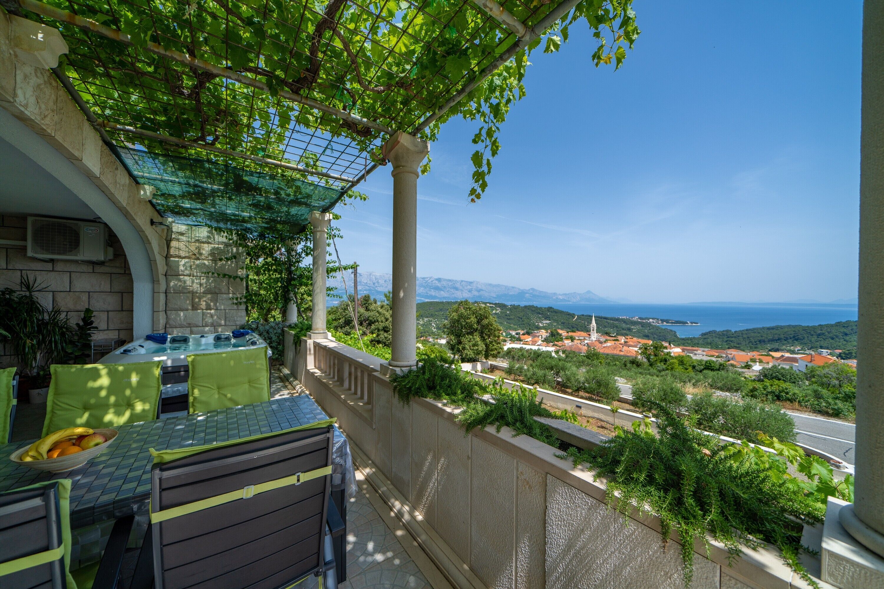 A terrace with a table and chairs, overlooking a scenic view of a coastal town and mountains.