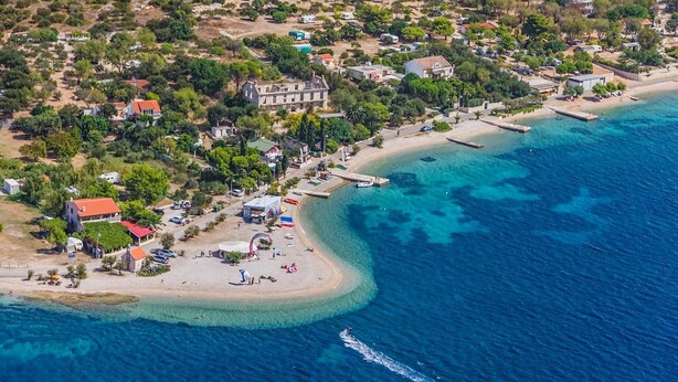 An aerial view of a coastal area with a beach, clear blue waters, and a mix of residential and commercial buildings. - Apartments Dijana - Studio Apartment with Terrace (Viganj)