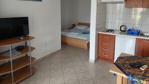 A compact hotel room with a bed, a television, a small kitchenette, and a bathroom visible through an open door. - Apartments Dijana - Studio Apartment with Terrace (Viganj)