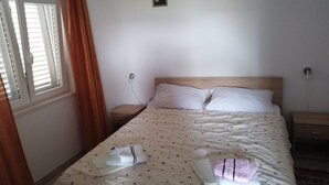 Un llit ben fet amb un sobrellit floral, una taula de nit amb una làmpada, i una finestra amb cortines.