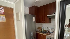 Een kleine keuken met houten kastjes, een roestvrijstalen koelkast, een spoelbak en een fornuis.