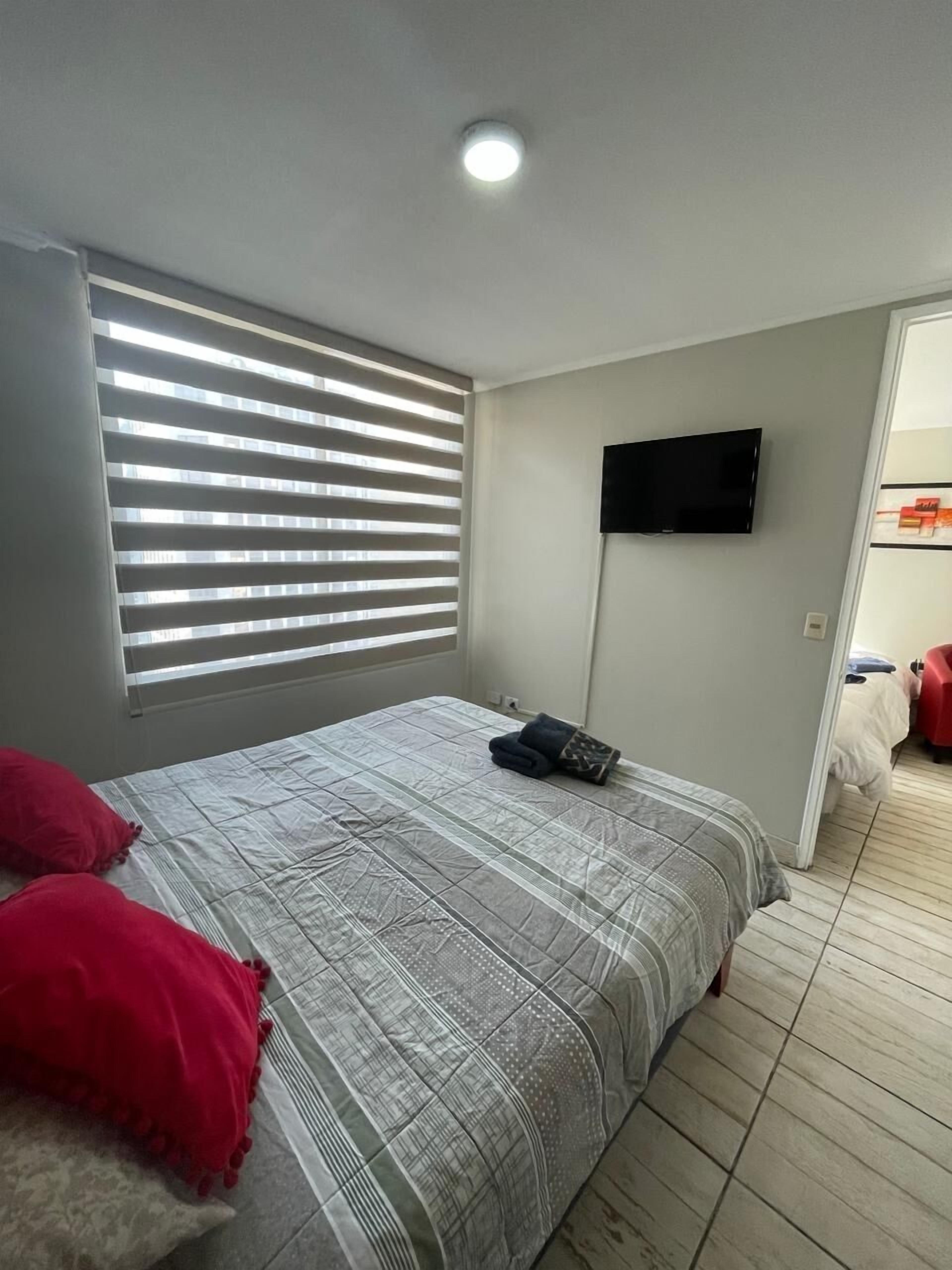 Une chambre à coucher avec un lit, un téléviseur fixé au mur et une fenêtre avec des stores.