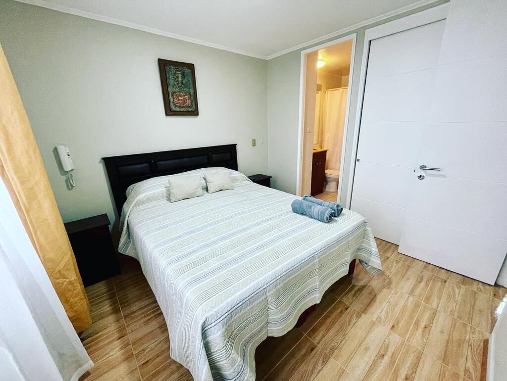 Une chambre à coucher avec un lit, une table de chevet, un téléphone, une porte et une salle de bain visible à travers une porte ouverte.