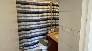 Een kleine badkamer met een gestreepte douchegordijn, een toilet en een wastafel met spiegel.