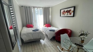 Een hotelkamer met twee bedden, een zithoek met een glazen tafel en stoelen, en een rode fauteuil.