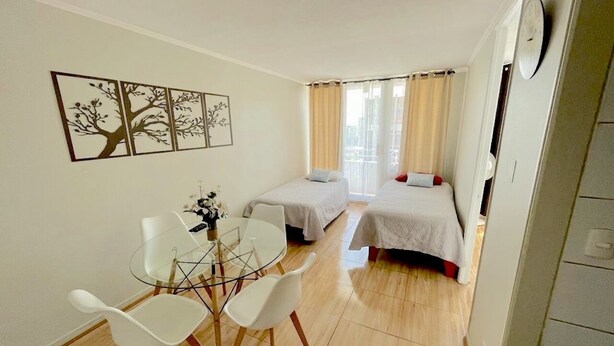 Een compacte, moderne kamer met een eettafel en stoelen, twee bedden en een klok aan de muur.