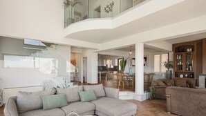A spacious living area with a large sectional sofa, a coffee table with plants, and a dining area with wooden chairs. - Villa Anemeli | Infinity pool ,sea view close to the city, Elite Crete II (Kissamos)