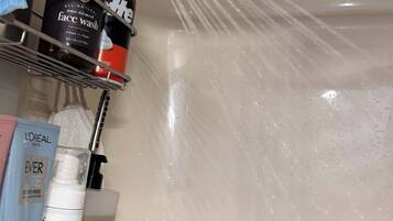 Un baño con ducha, un estante con artículos de aseo y una bañera.