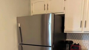 Ein Edelstahl-Kühlschrank in einer Küche mit weißen Schränken und einer Arbeitsplatte aus Granit.