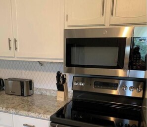Una cucina con mobili bianchi, un tostapane, un portachiodi e un forno in acciaio inossidabile.