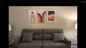 Ein graues Sofa mit zwei Kissen, eine Wand mit abstrakter Kunst und eine Lampe auf jeder Seite.