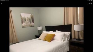 Ein Hotelzimmer mit Bett, Nachttisch, Lampe und einem Gemälde an der Wand.