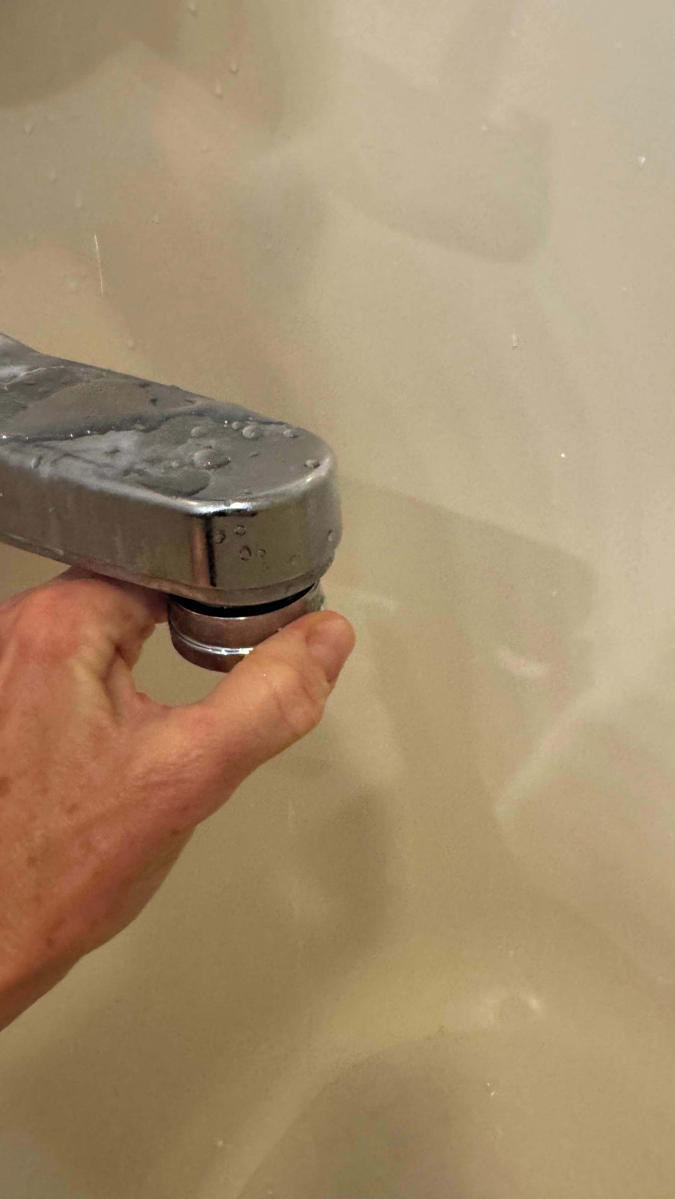 A hand holding a faucet with water running.