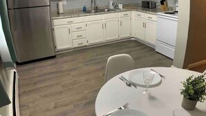 Une cuisine moderne avec des meubles blancs, des appareils en acier inoxydable et un coin repas avec une table blanche mise pour deux personnes.