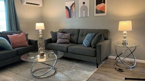Un salon moderne avec un canapé gris, deux tables d’appoint et des œuvres d’art abstraites accrochées au mur.