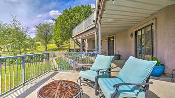 Relax on the balcony with a fire pit, two comfortable chairs, and a potted plant overlooking a serene landscaped area.