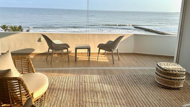 A balcony with a view of the ocean, wicker furniture, and a woven rug. - U-GO Faro Tequendema (Cartagena)