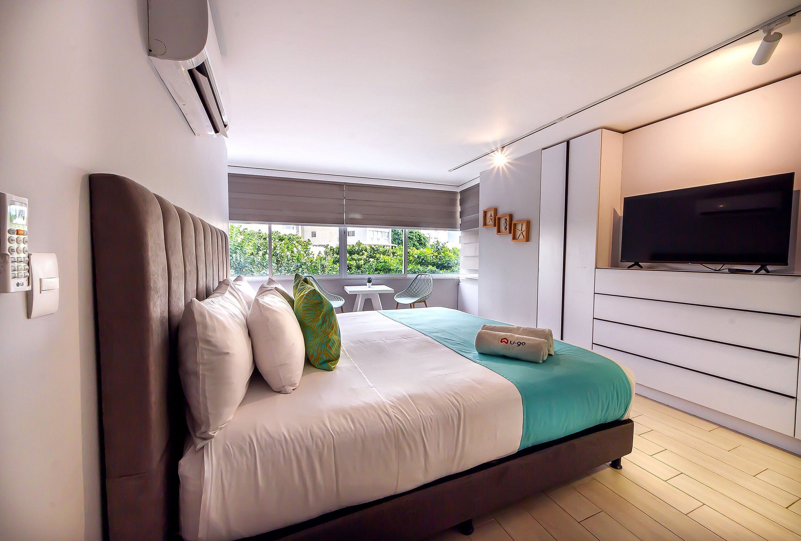A modern bedroom with a large bed, a television, and a view of greenery outside.