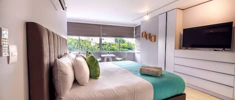 A modern bedroom with a large bed, a television, and a view of greenery outside.