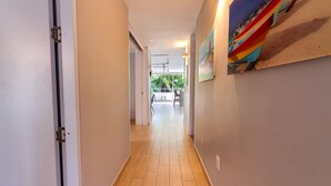 A hallway with a wooden floor, white walls, and a door on the left. There is a window at the end of the hallway. - U-GO Faro Tequendema (Cartagena)