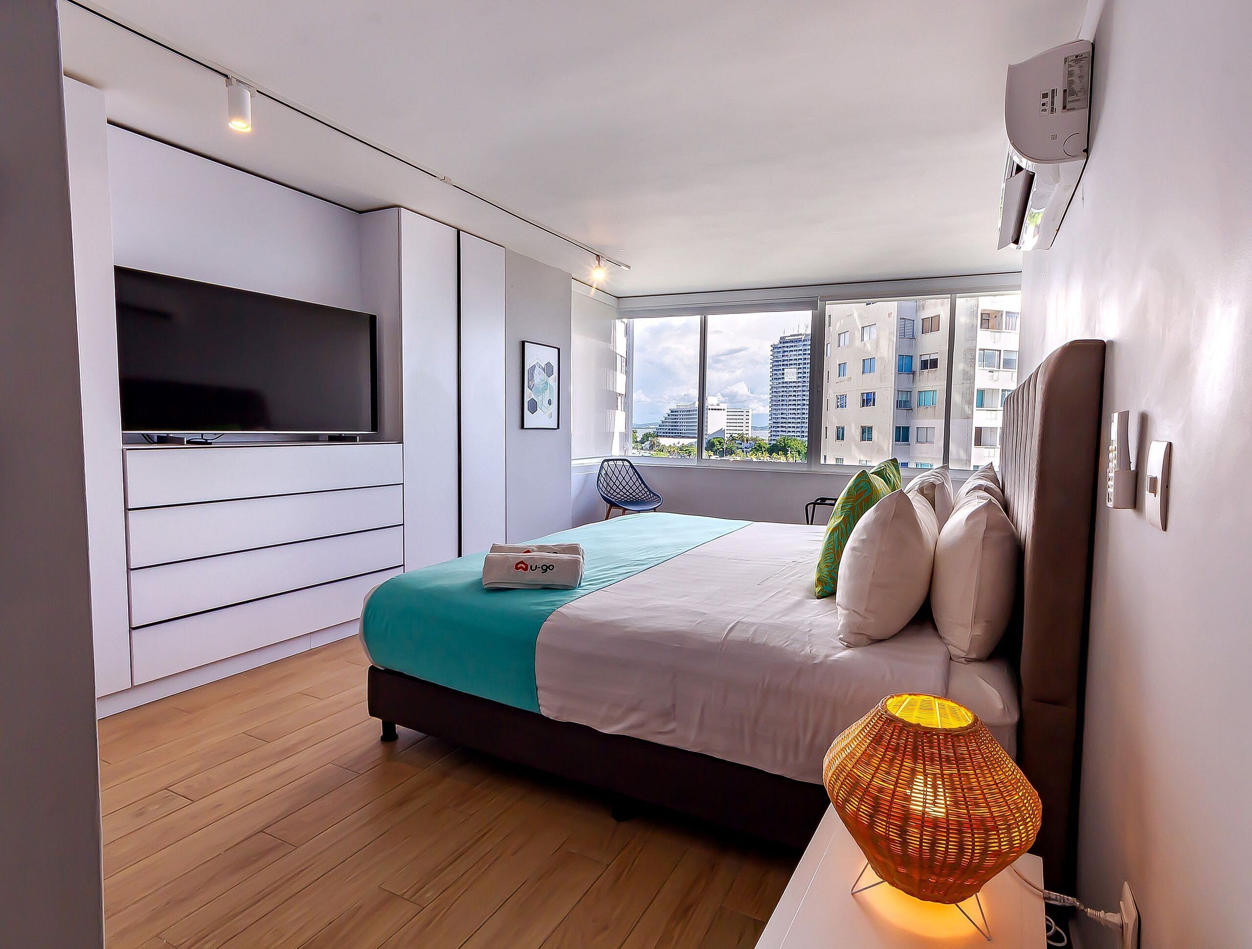 A modern hotel room with a bed, a television, and a view of the cityscape.