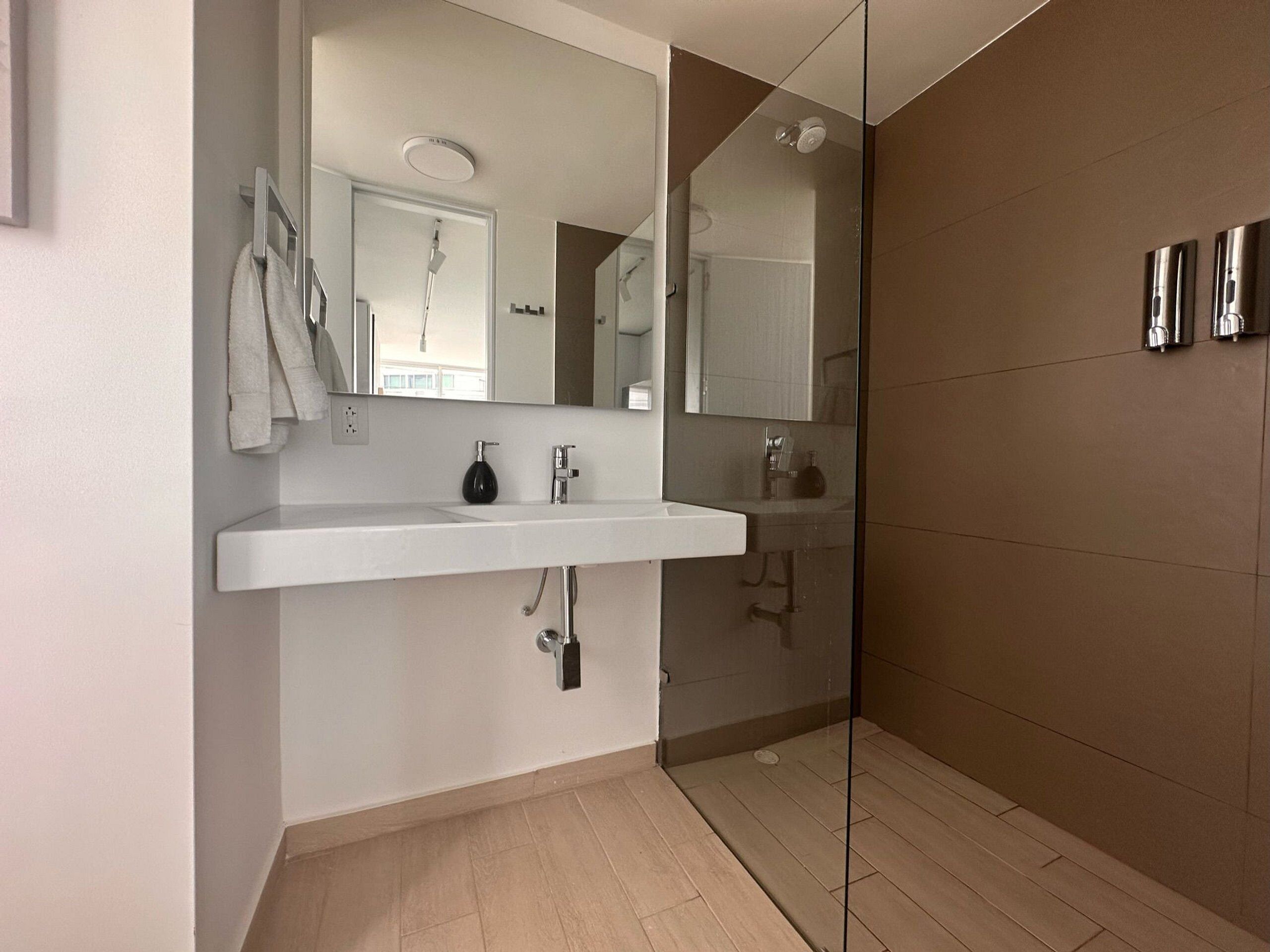 Ein modernes Badezimmer mit einem weißen Waschbecken, einem Spiegel und einer Duschkabine aus Glas.