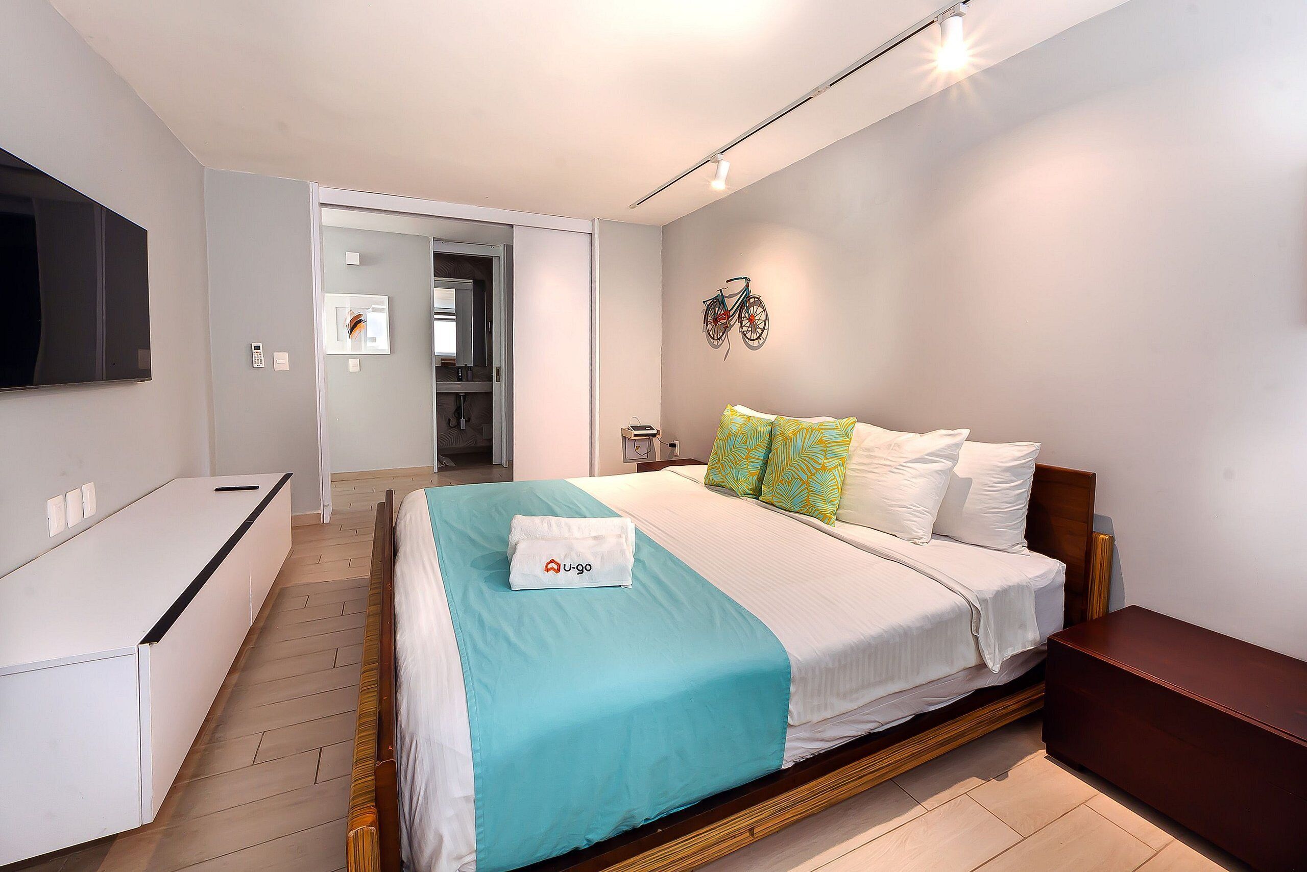 A hotel room with a bed, bedside table, and a television mounted on the wall.