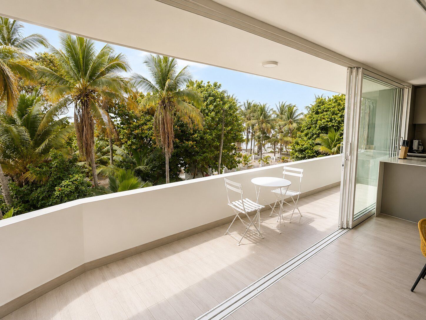 Ein Balkon mit Blick auf Palmen, einem Tisch mit Stühlen und einer Schiebetür.