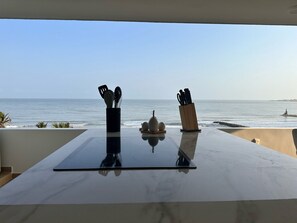 A table with kitchen utensils and a decorative item, overlooking a beach with calm waters and a clear sky. - U-GO Faro Tequendema (Cartagena)