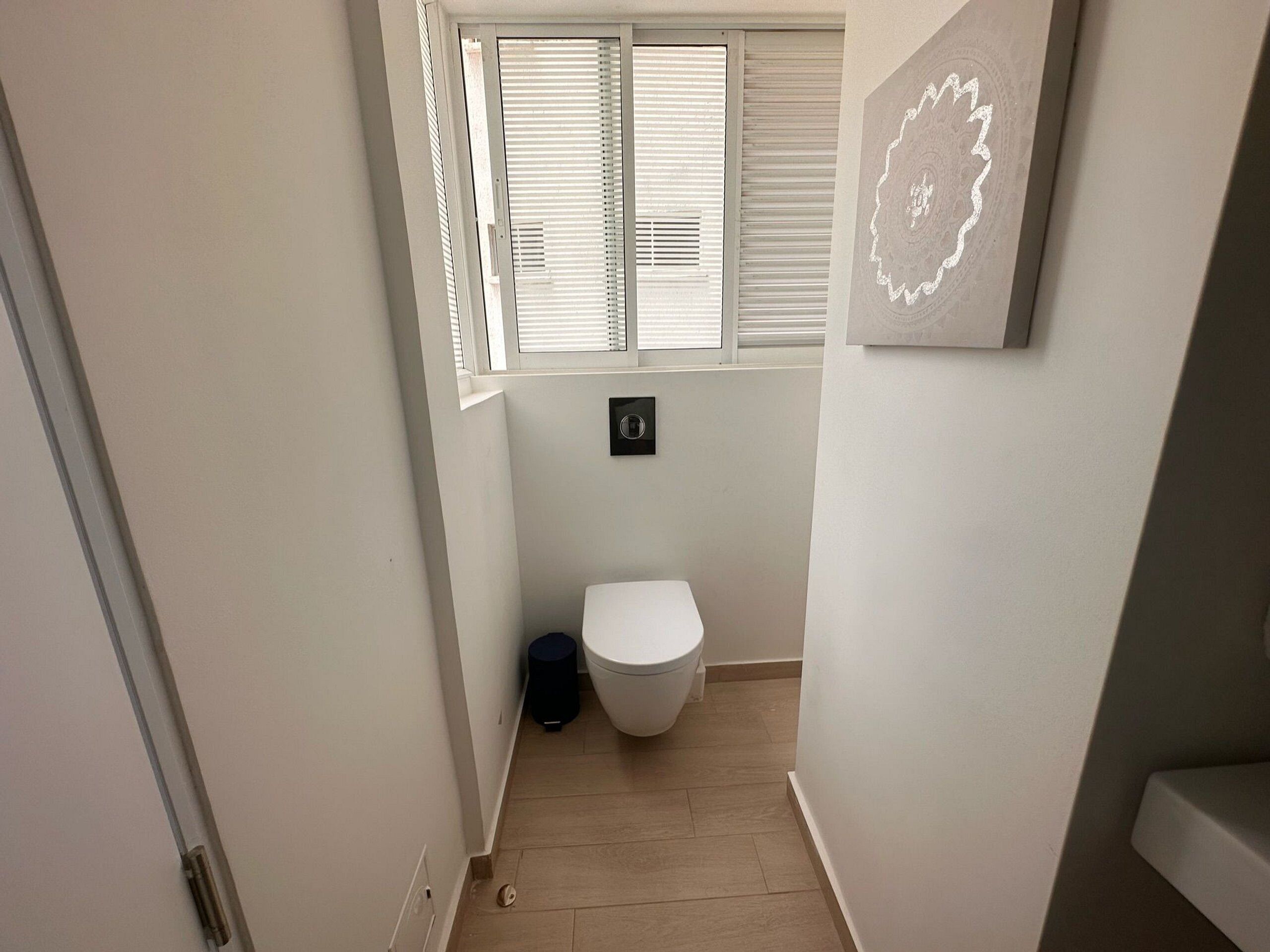 Un baño estrecho con un inodoro, una ventana con persianas y un interruptor de luz en la pared.