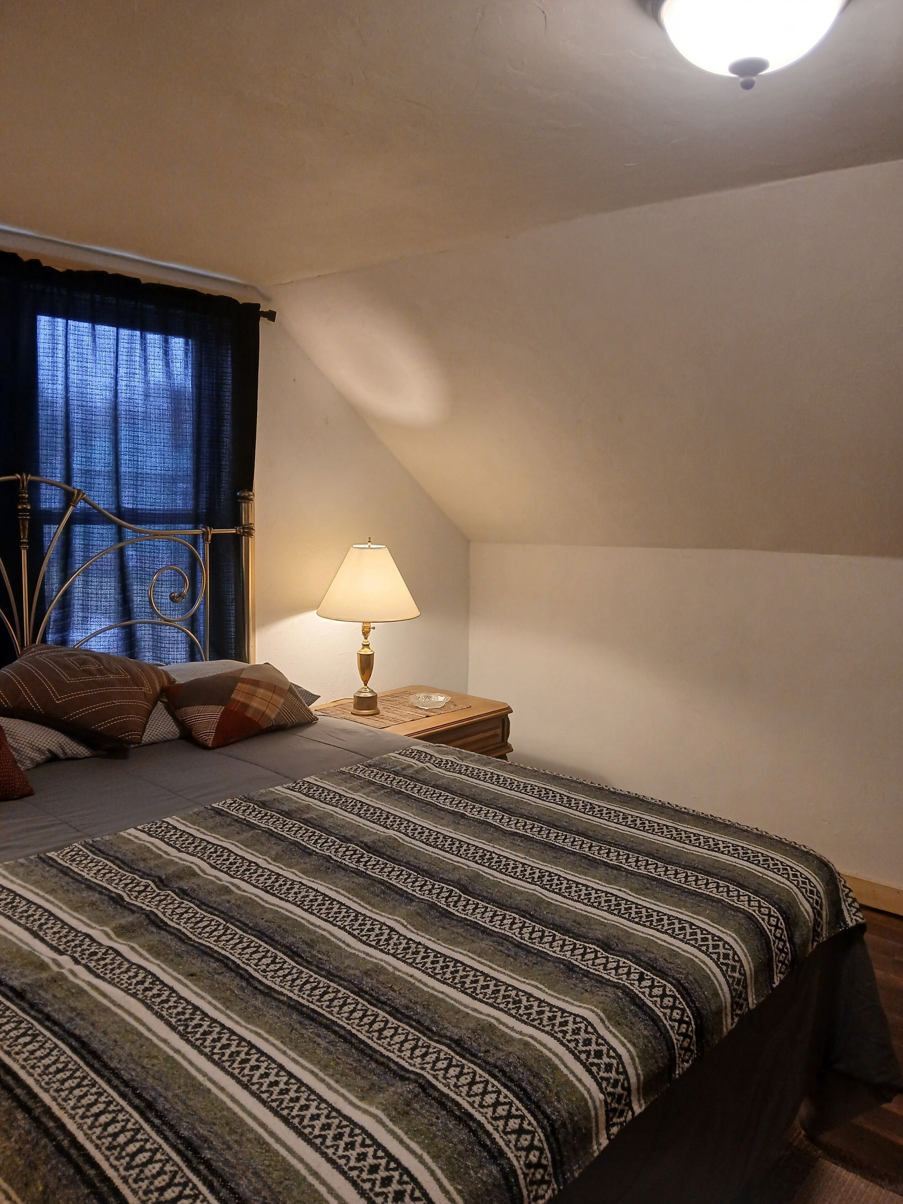 Ein Schlafzimmer mit einem Bett, einem Nachttisch, einer Lampe und einem Fenster mit Vorhängen.