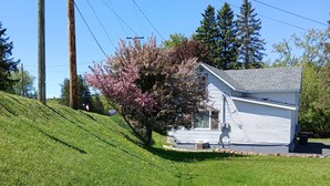 Une maison avec un toit en pente, un porche et une cour avec de la pelouse et un arbre en fleurs.