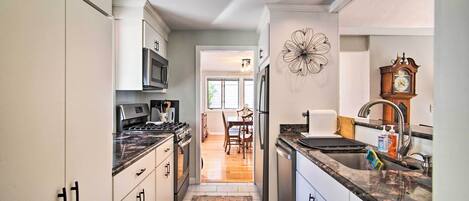 A kitchen with white cabinets, a stainless steel refrigerator, a microwave, and a stove. There is a rug on the floor and a clock on the wall.