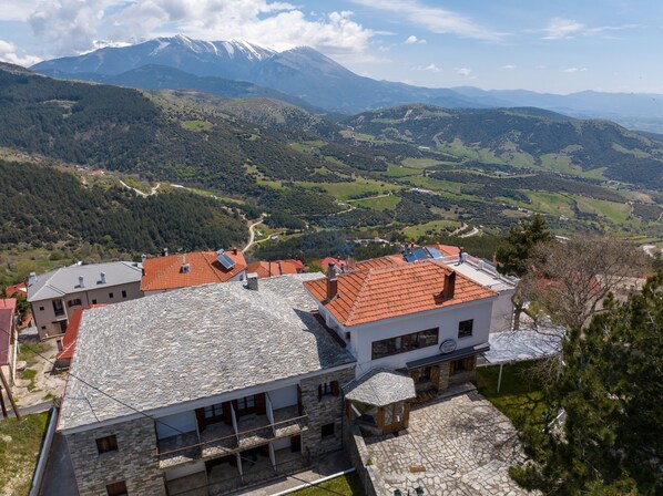 A stone building with a red-tiled roof, a wooden balcony, and a stone pathway leading to a gazebo. - Hotel Mitikas (Elassona)