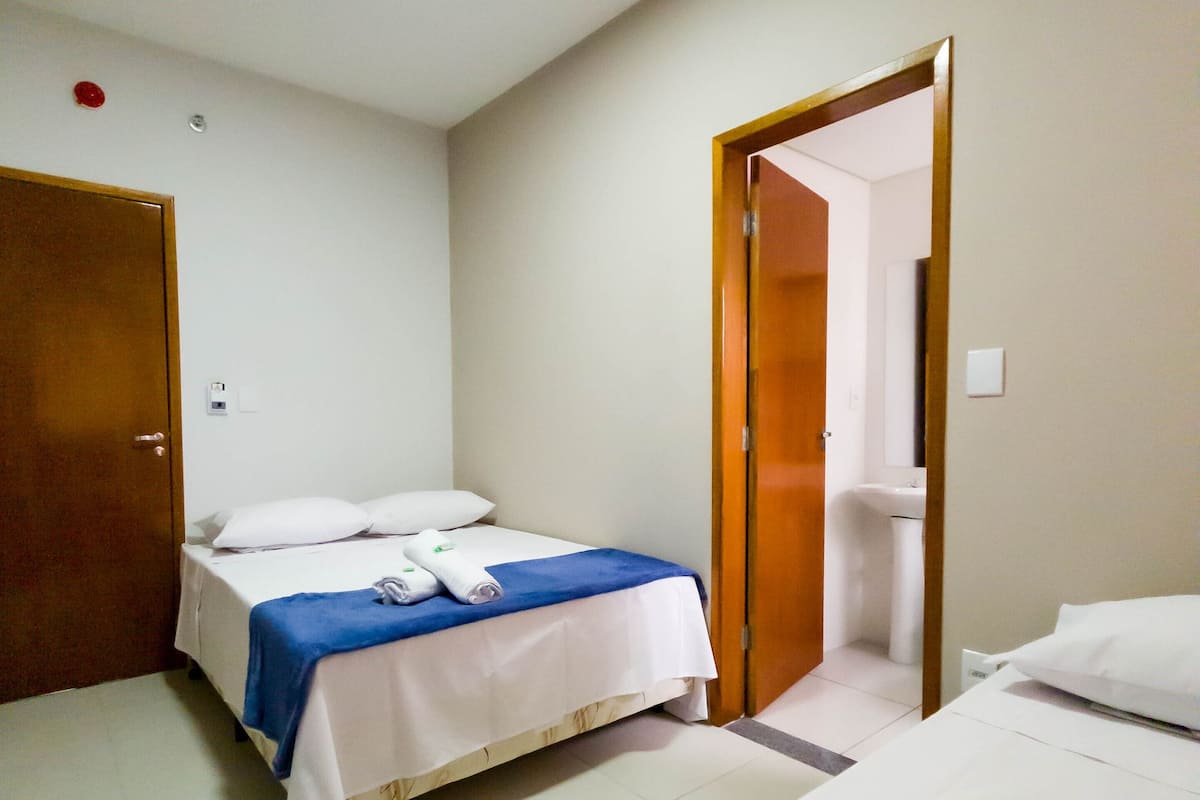 Quarto de hotel com duas camas, banheiro e porta de madeira.