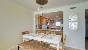 A dining area with a wooden table and benches, a kitchen in the background, and a decorative mirror on the wall. - Luxury Oceanfront Couples Retreat- Station 1 Top Floor, Newly Renovated (Wrightsville Beach)