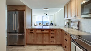 A modern kitchen with wooden cabinets, stainless steel appliances, and a large island. - Luxury Oceanfront Couples Retreat- Station 1 Top Floor, Newly Renovated (Wrightsville Beach)