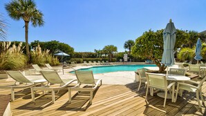 A poolside area with lounge chairs and umbrellas, surrounded by palm trees and greenery. - Luxury Oceanfront Couples Retreat- Station 1 Top Floor, Newly Renovated (Wrightsville Beach)