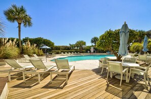 A poolside area with lounge chairs and umbrellas, surrounded by palm trees and greenery.