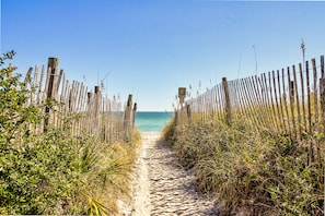 Ein sandiger Pfad, der von Holzzaunen gesäumt wird und zu einem Strand führt.