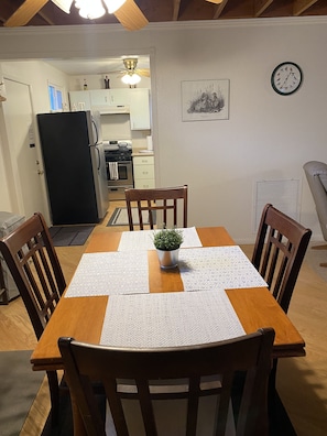 Enjoy meals in this cozy dining area with a table for four, a potted plant, and a kitchen in the background.